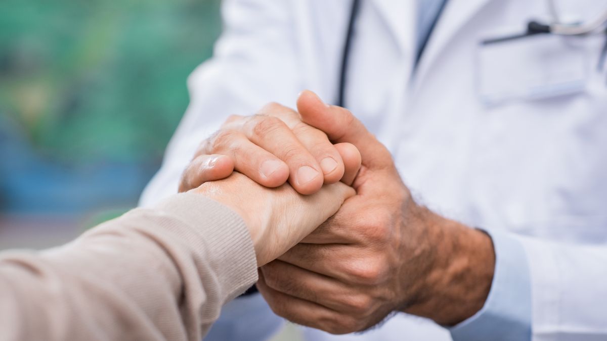 A doctor holding the hand of a patient to signify patient care